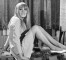 Wendy Richard, wearing a light-colored mini-dress and long wig, lounging on a blanket