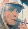 Wendy Richard wearing a ball cap and puffing on a cigarette holder, circa 1978.