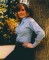 Wendy Richard leaning against a tree, wearing slacks and a striped shirt