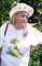 Wendy Richard, outdoors, smilling.  Casually dressed:  fFrog T-shirt, big sunhat with frog pins.
